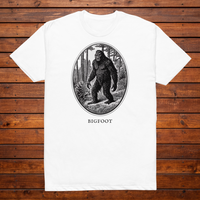 Bigfoot engraved cryptid t-shirt — black and white crosshatch medallion design on white tee, flat lay