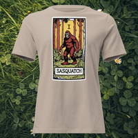 Bigfoot tarot card design on Heather Stone t-shirt flat lay on grass — Lost Arcana series by Cryptid Emporium