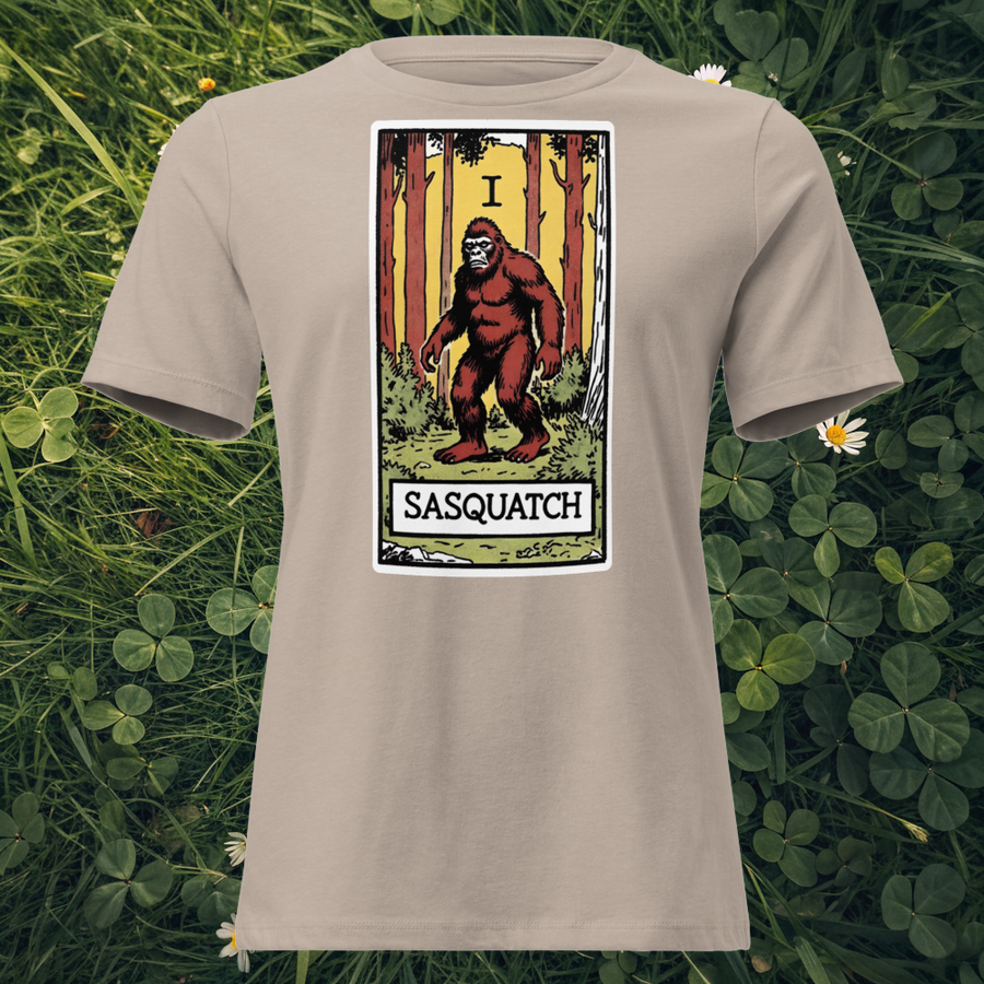Bigfoot tarot card design on Heather Stone t-shirt flat lay on grass — Lost Arcana series by Cryptid Emporium